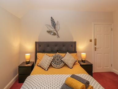 A bedroom with a bed with patterned pillows and yellow bedding with two bedside tables with lamps and a door at Tudor House in Symonds Yat