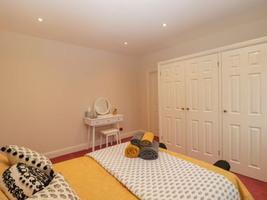 A bedroom with a bed covered in yellow and white linens with rolled towels on top a white vanity table and stool against the wall and white double closet doors at Tudor House in Symonds Yat
