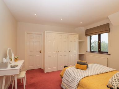 A bedroom with a bed covered with yellow and patterned bedding alongside a white dressing table with a mirror and stool at Tudor House in Symonds Yat