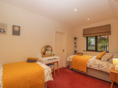 A bedroom with two single beds yellow bedspreads and a dressing table by the door at Tudor House in Symonds Yat