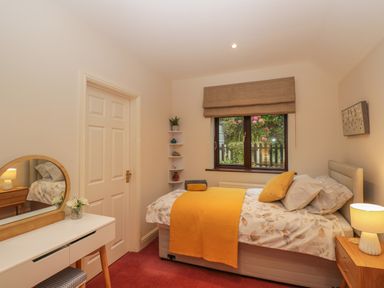 A bedroom with a bed covered with floral bedding and yellow throw blanket next to a window with plants outside at Tudor House in Symonds Yat