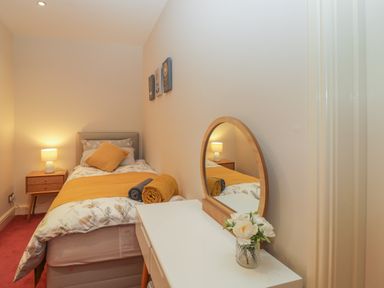 A bedroom with a single bed a bedside table and a dressing table with a mirror and flowers at Tudor House in Symonds Yat