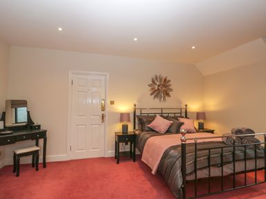 A bedroom with a black metal bed frame pink and gray bedding two bedside tables with lamps a dressing table with mirror and stool at Tudor House in Symonds Yat