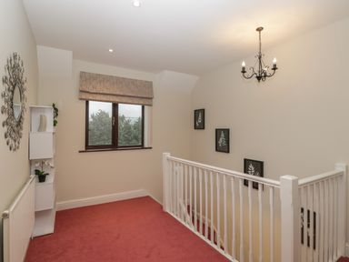 A stair landing with a white banister red carpet a window with patterned blind wall art and a shelf with decorations at Tudor House in Symonds Yat