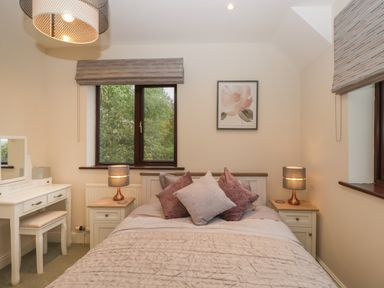 A bedroom with a bed and pillows between two lamps and a dressing table by a window at Tudor House in Symonds Yat