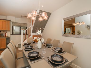 A dining table set with plates and glasses with chairs around in a room with a staircase and a mirror at Tudor House in Symonds Yat