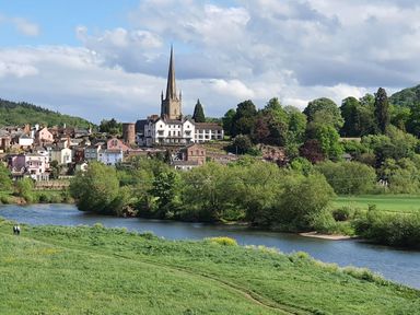 A riverside town with a church with a tall spire surrounded by trees and houses at Tudor House in Symonds Yat