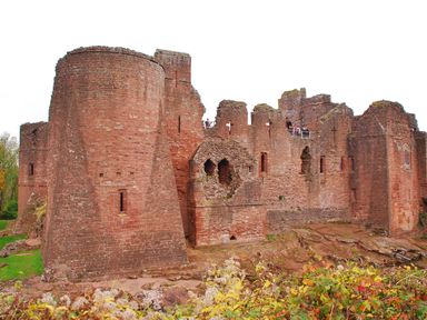 A large stone castle ruin with rounded towers and arched windows surrounded by greenery at Tudor House in Symonds Yat