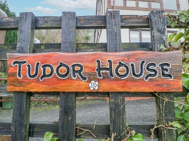 A wooden sign with Tudor House written on it attached to a black wooden fence with a house in the background at Tudor House in Symonds Yat