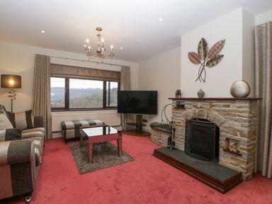 A living room with a striped sofa ottoman glass coffee table stone fireplace and television at Tudor House in Symonds Yat