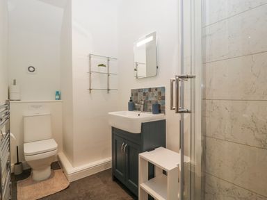 A bathroom with a toilet a sink with blue cabinet a glass shower enclosure and a small white shelf at Tudor House in Symonds Yat