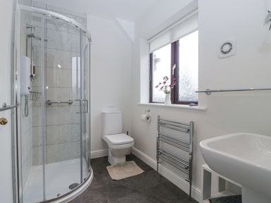 A bathroom with a curved glass shower enclosure a toilet a sink a window with a vase of flowers and a heated towel rail at Tudor House in Symonds Yat