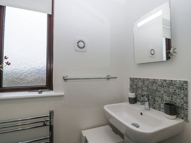 A bathroom with a sink mirror tiled backsplash towel rail and frosted window at Tudor House in Symonds Yat