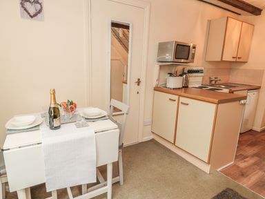 A small kitchen area with a dining table set for two and kitchen appliances at Robin Cottage in Morpeth