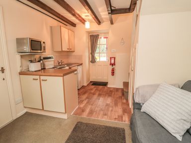A small kitchen area with microwave oven toaster kettle and stove next to a door with window and a sofa with cushions and blanket at Robin Cottage in Morpeth