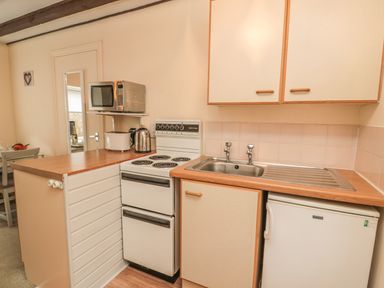 A kitchen with a stove a microwave a kettle a toaster a sink and cabinets at Robin Cottage in Morpeth