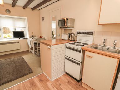 A small kitchen with a stove sink microwave and a dining table with two chairs near a window at Robin Cottage in Morpeth