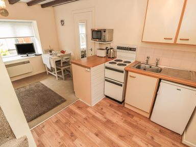 A kitchen area with stove microwave toaster and sink next to a small dining table and television at Robin Cottage in Morpeth