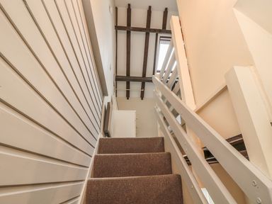 A staircase with carpeted steps white wooden railing and exposed ceiling beams at Robin Cottage in Morpeth