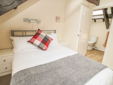 A bedroom with a bed white bedding a checkered pillow bedside tables and an open door to a bathroom at Robin Cottage Morpeth