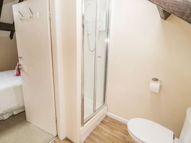 A bathroom with a toilet shower and open door showing a bed in bedroom at Robin Cottage in Morpeth