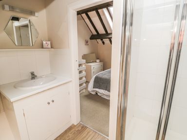 A bathroom with a sink and mirror next to a shower and an open door showing a bedroom with exposed beams at Robin Cottage in Morpeth