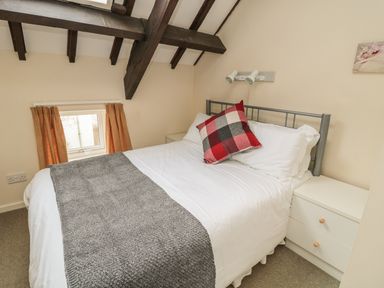 A bedroom with a bed with white sheets and a gray blanket under a ceiling with exposed wooden beams at Robin Cottage in Morpeth