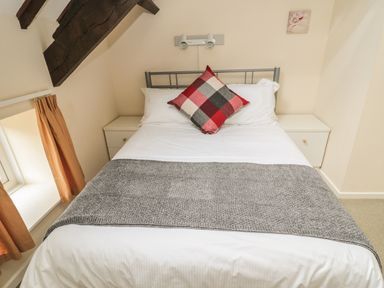 A bedroom with a double bed flanked by two white nightstands and brown curtains on a window at Robin Cottage in Morpeth