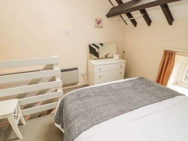 A bedroom with a bed a white dresser and a window with curtains at Robin Cottage in Morpeth
