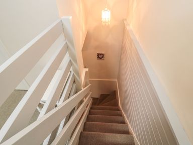 A carpeted staircase with white wooden railings and a hanging ceiling light at Robin Cottage in Morpeth