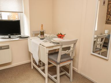 A small dining table set for two with plates glasses a bottle of champagne and a bowl of tomatoes next to a window with a television on the windowsill at Robin Cottage in Morpeth