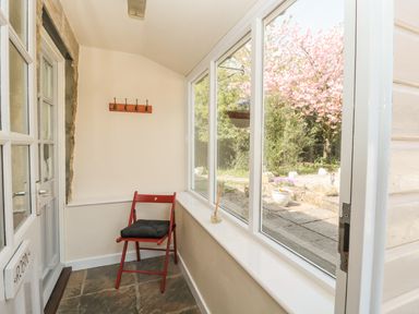A small enclosed porch with a red chair and stone floor looking out to a garden with pink flowering tree at Robin Cottage in Morpeth