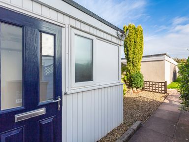 The exterior of a building with a dark blue door a frosted window a pathway gravel and greenery at 164 Cumber Close in Malborough