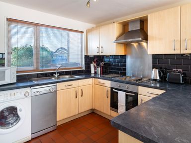 A kitchen with wooden cabinets black countertops a washing machine dishwasher stove oven kettle toaster and a window at 164 Cumber Close in Malborough