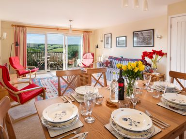 A dining table set with plates and glasses in a living room with red chairs and a striped sofa at 164 Cumber Close in Malborough