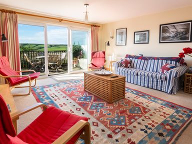 A living room with red chairs striped sofa and a wooden coffee table next to sliding glass doors at 164 Cumber Close in Malborough
