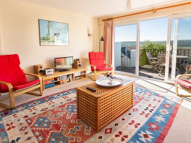 A living room with red chairs a patterned rug a low wooden cabinet with a television and sliding glass doors leading to a patio at 164 Cumber Close in Malborough