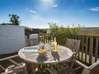 An outdoor wooden table with chairs bowls of crisps and bottles on a patio with countryside view at 164 Cumber Close in Malborough