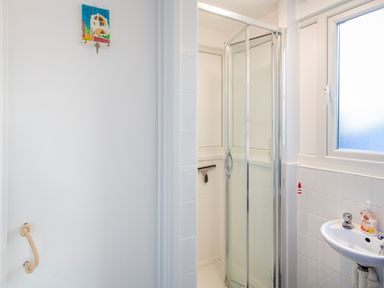 A bathroom with a corner shower, a white sink, a frosted window, and a door with a rope handle at 164 Cumber Close in Malborough