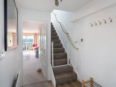 A hallway with carpeted stairs and a safety gate leading to a living room with a red chair and sliding glass doors at 164 Cumber Close in Malborough