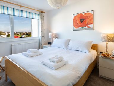 A bedroom with a bed with white linens towels on top a painting of a poppy flower on the wall and a window with striped blinds at 164 Cumber Close Malborough