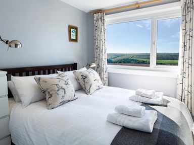 A bedroom with a bed with folded towels and bird patterned pillows near a window with countryside view at 164 Cumber Close in Malborough