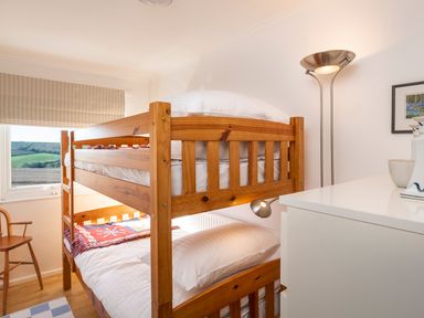 A bedroom with wooden bunk beds a wooden chair a floor lamp and a white dresser at 164 Cumber Close in Malborough