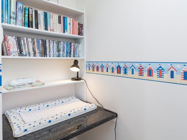 A changing table with a star-patterned pad under shelves holding books and DVDs in a room with a wall border of beach huts at 164 Cumber Close in Malborough