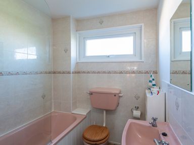 A bathroom with a pink bathtub toilet and sink with a window above the toilet at 164 Cumber Close in Malborough