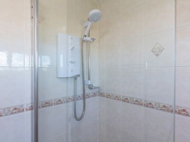 A tiled shower enclosure with an electric shower unit and handheld showerhead at 164 Cumber Close in Malborough