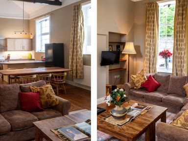 A living room with a brown sofa and wooden coffee table with flowers and books next to a kitchen area with a wooden dining table and chairs at The Old School in Gortin