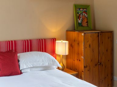 A bedroom with a striped headboard red pillows white bed linens a lamp on a bedside table wooden wardrobe with a painting on top at The Old School in Gortin