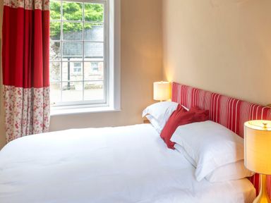 A bedroom with a bed with white linens red pillows and a striped headboard beside a window with red and floral curtains at The Old School in Gortin