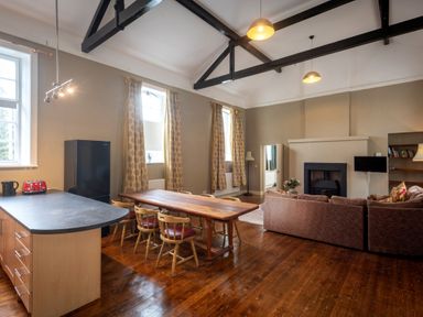 An open-plan living room with a kitchen island, dining table with chairs, sofa, and fireplace at The Old School in Gortin